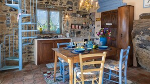 A rustic kitchen with a blue spiral staircase, a wooden dining table with chairs, and a chandelier. - Azzurra (PTB145) by Interhome (Pietrabruna)