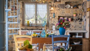 A rustic kitchen with stone walls, a wooden table, and a blue vase with flowers. - Azzurra (PTB145) by Interhome (Pietrabruna)