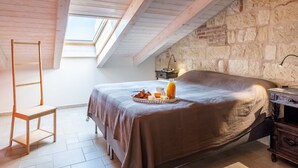 Un dormitorio acogedor con techo inclinado, una escalera de madera, una cama con una bandeja de desayuno y una pared de piedra.