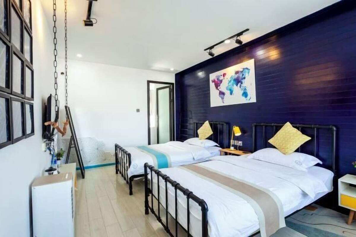 A hotel room with two beds, a dark blue accent wall, a map artwork, and a small table with a lamp.