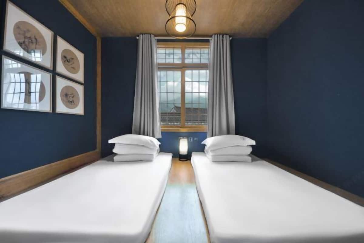 A room with two beds, a window with curtains, and framed pictures on the wall.