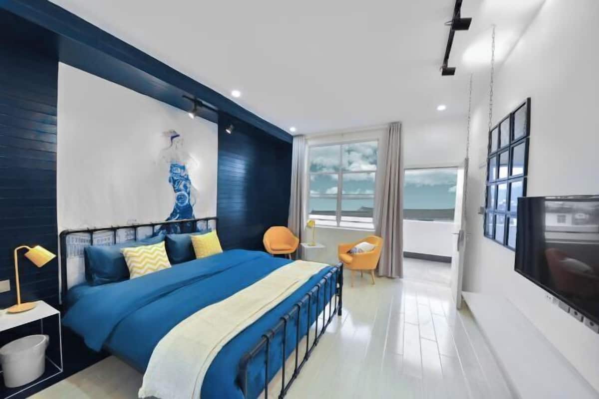 A modern bedroom with a bed, a TV, a chair, and a window.