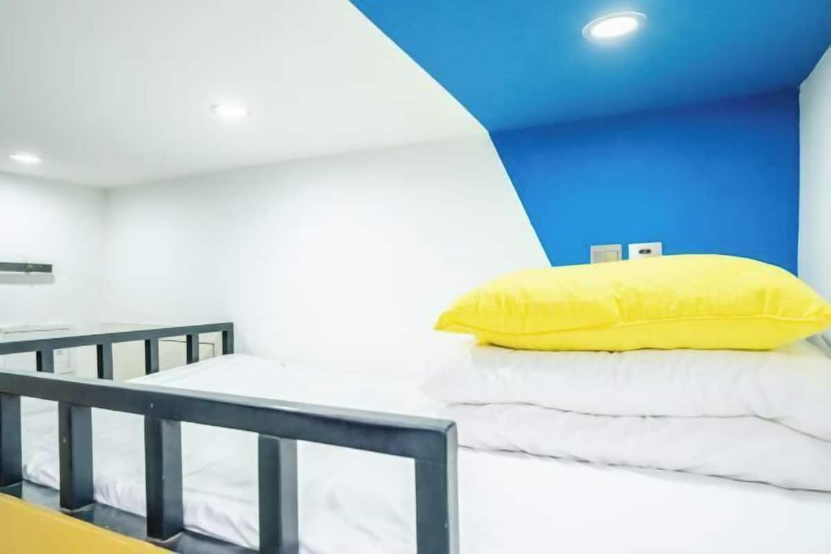 A room with a bunk bed, white bedding, a yellow pillow, and a blue accent wall.