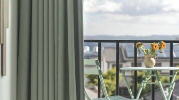 A balcony with a table and chairs, a vase with flowers, and a view of buildings and a cloudy sky.