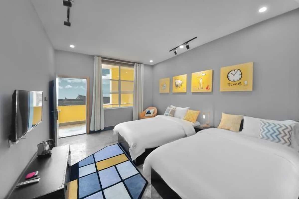 A hotel room with two beds, a TV, a desk, and a window with a view.
