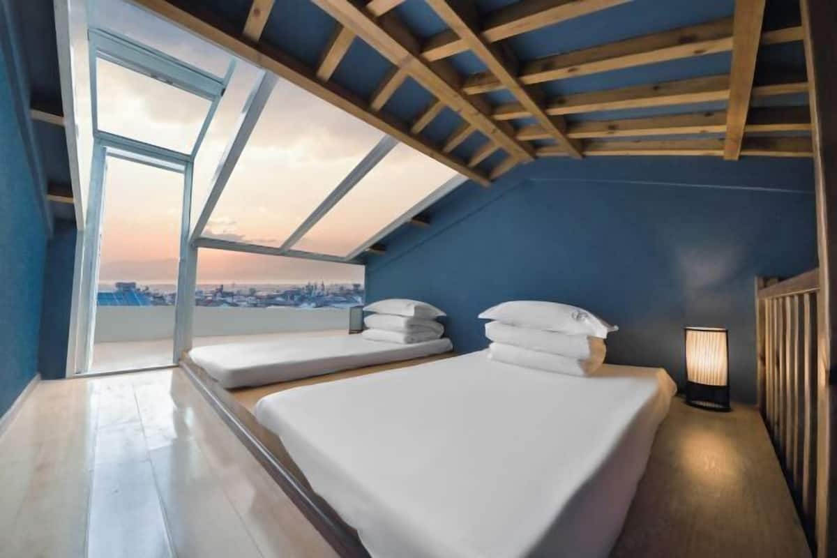 A room with two beds, a skylight, a city view, and a bedside lamp.