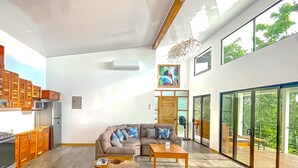 A spacious living area with a large sofa, a coffee table, and a kitchen area with wooden cabinets and a built-in microwave. - Casa Toucan (Bahía Ballena)