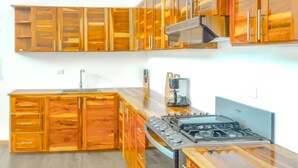 A modern kitchen with wooden cabinets, a gas stove, and a coffee maker. - Casa Toucan (Bahía Ballena)