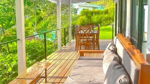 A wooden deck with a sofa and table, surrounded by lush greenery. - Casa Toucan (Bahía Ballena)