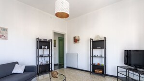 Ein modernes Wohnzimmer mit einem grauen Sofa, einem runden Glastisch, schwarzen Regaleinheiten und einem Flachbildfernseher.