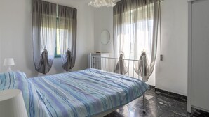 Ein Schlafzimmer mit Bett, Nachttisch, Lampe, Spiegel und Vorhängen.