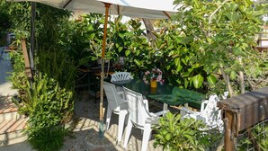 A patio with a table and chairs under a white umbrella, surrounded by lush greenery and a clear sky. - Francesca by Interhome (Sanremo)