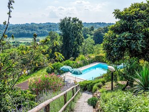A pool surrounded by lush greenery and a view of distant hills. - Bricco dei Ciliegi by Interhome (Cortazzone)