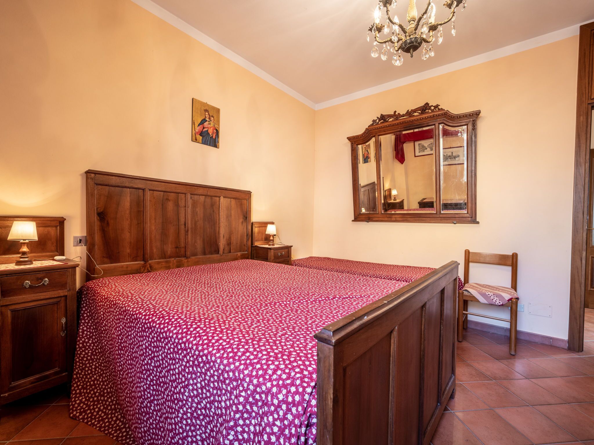 A bedroom with a wooden bed, a nightstand, a chair, a mirror, and a chandelier.