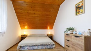 A bedroom with a wooden ceiling, a bed with a white cover, bedside lamps, a wooden dresser, and a framed picture on the wall. - Rakoczi by Interhome (Balatonmariafurdo)