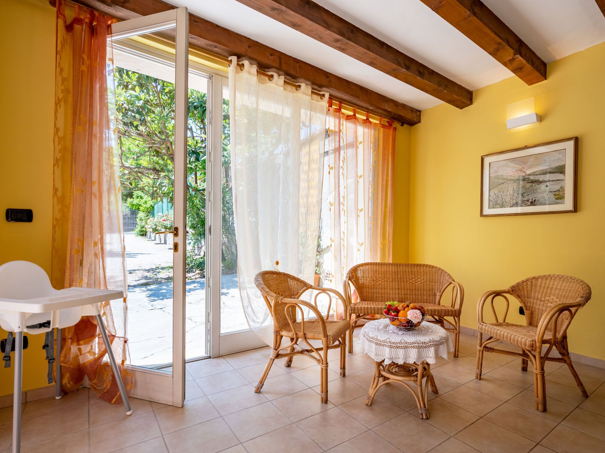 Habitació amb cadires de vimetla, una taula petita amb un plat de fruita i una vista a través d'una porta de vidre a una zona exterior.
