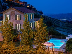 A villa with a swimming pool, surrounded by trees and overlooking a vineyard.