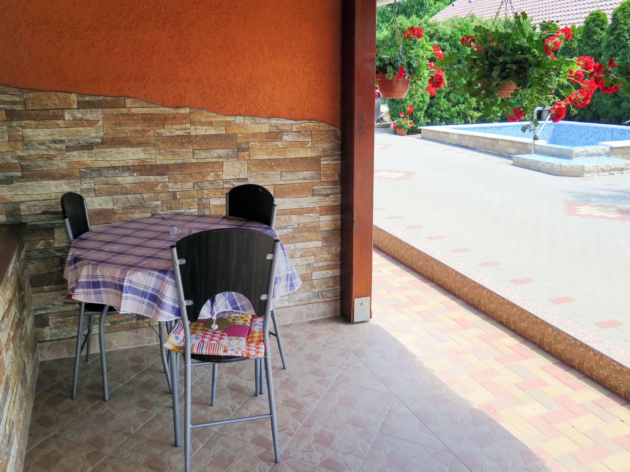 Un patio techado con una mesa y sillas, un muro de piedra y vistas a una piscina y jardín.