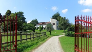 A gravel path leading to a white building with a red roof, surrounded by greenery and a red metal gate.