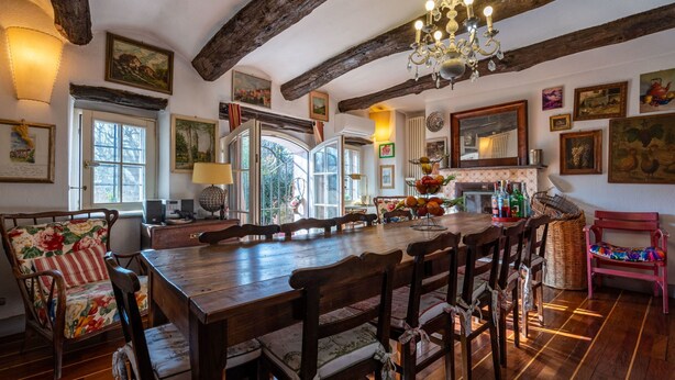 Un comedor espacioso con una gran mesa de madera y sillas, una araña y diversas obras de arte en las paredes.