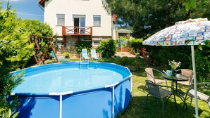 Una casa con piscina, terraza de madera y patio con mobiliario exterior.
