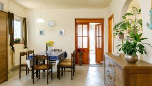 Un comedor con una mesa dispuesta para cuatro, sillas de madera, un reloj en la pared y una puerta que da a otra habitación.