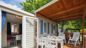 Un espace extérieur abrité, aménagé pour les repas, avec une table et des chaises, une entrée couverte et une vue sur la végétation environnante.