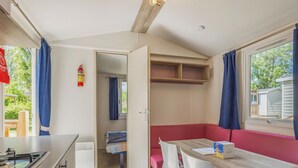 Une cuisine compacte équipée d’une cuisinière, d’un coin repas avec une table et des chaises, d’un banc rouge et d’une fenêtre avec des rideaux.