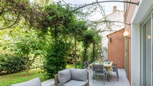 A patio with a sofa, table, and chairs, surrounded by greenery and a building. - Les Rives du Golf 3 by Interhome (Roquebrune sur Argens)