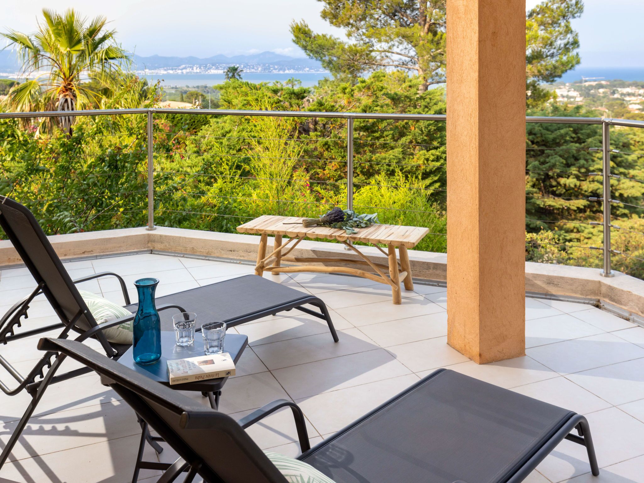 A terrace with a table, chairs, and a view of the sea and mountains.