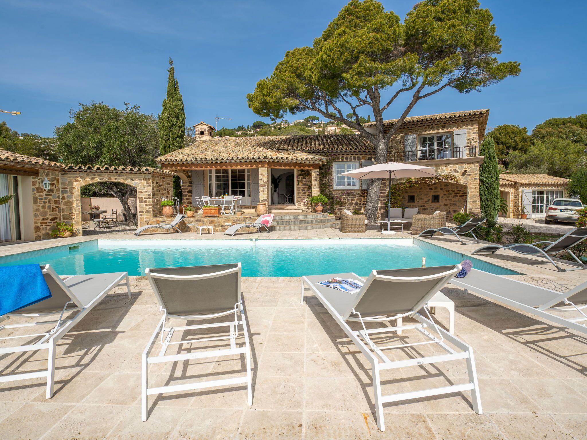 A stone villa with a swimming pool, outdoor seating, and a large tree.