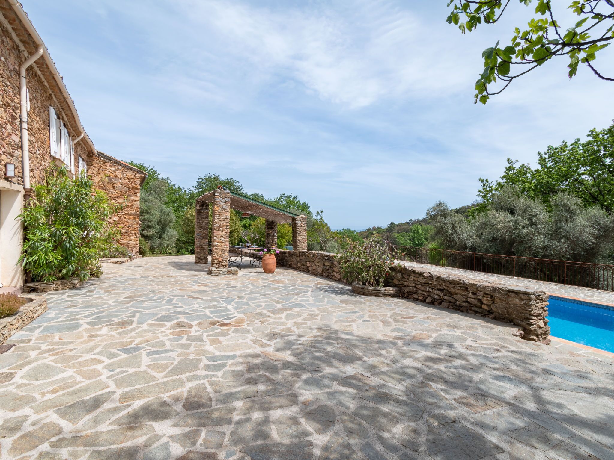 A stone patio with a pergola, a swimming pool, and a stone building with windows.