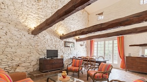 A rustic interior with stone walls, wooden beams, wicker furniture, and a dining area with a table and chairs. - La Bastide Haute by Interhome (La Garde Freinet)