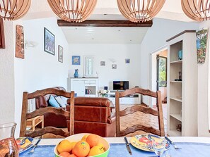 A dining area with a table set for four, a bowl of fruit, and a television in the background. - Le Mas d'Olive by Interhome (Grimaud)