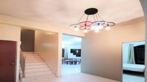 A spacious hallway with a staircase leading to a dining area, a bed, and a modern ceiling light fixture. - OYO 91031 House No 8 (Muar)