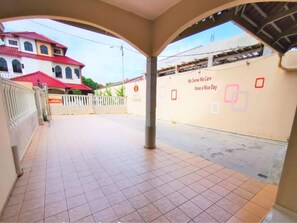 A covered outdoor area with tiled flooring, a white fence, and a building with a red roof in the background. - OYO 91031 House No 8 (Muar)