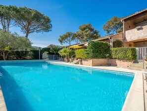 Relax by the serene pool surrounded by lush greenery and mature trees, with a covered seating area nearby.
