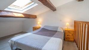 A bedroom with a skylight, a bed with a striped bedspread, two bedside tables with lamps, and wooden headboards.