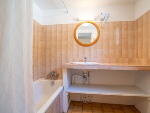 Bathroom features a bathtub, sink, and shelf, with a mirror above.
