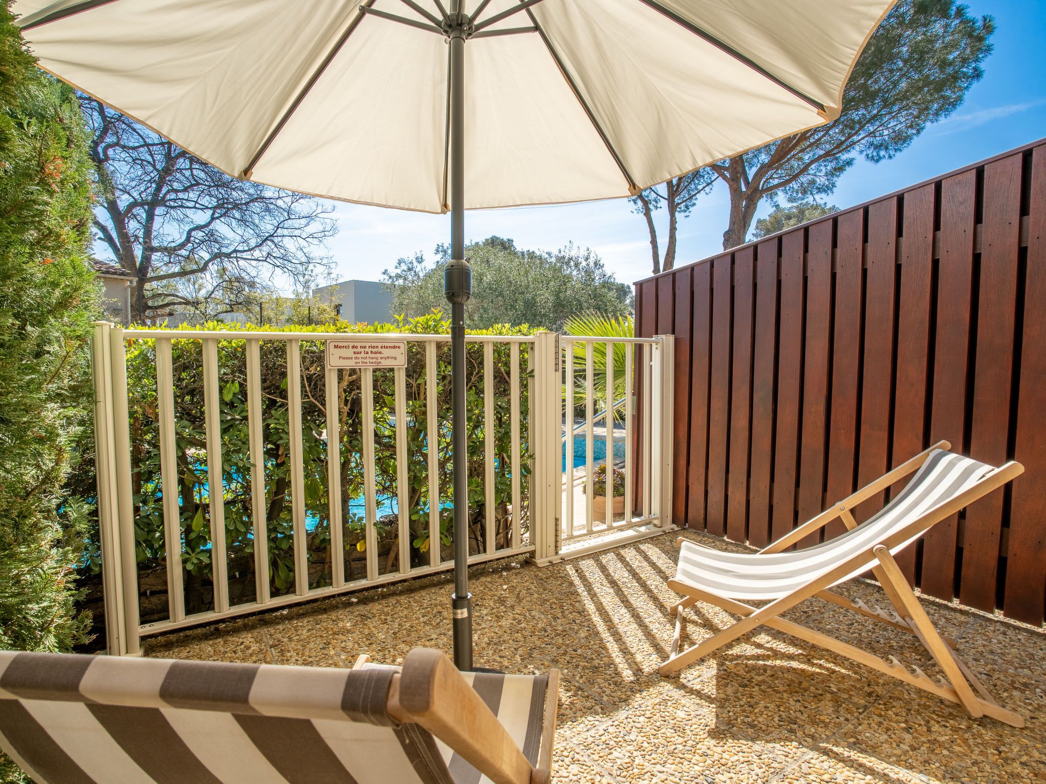 Eine Terrasse mit Pool, Holzzaun und einer Liege unter einem großen Sonnenschirm.