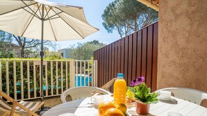 A round table with white chairs, a beige umbrella, and a bottle of orange juice.