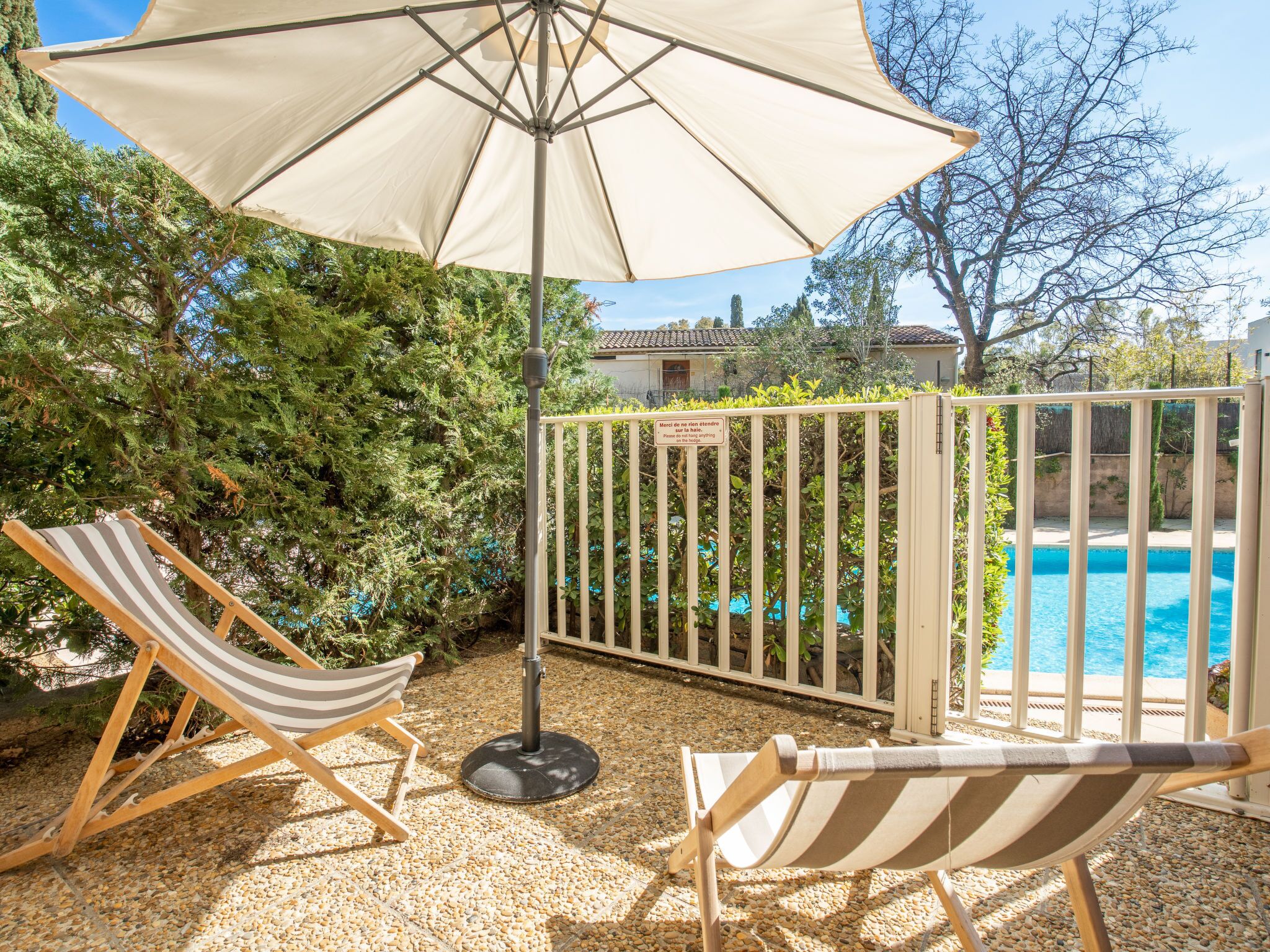 Un espace aménagé au bord de la piscine, avec deux chaises longues à rayures, un parasol beige et une vue sur la piscine.