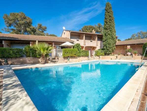 Relax by the serene pool surrounded by lush greenery and a Mediterranean-style building.