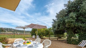 An outdoor dining area with a round table and chairs, surrounded by gravel, under a large umbrella. - Villa Marenco by Interhome (La Croix-Valmer)