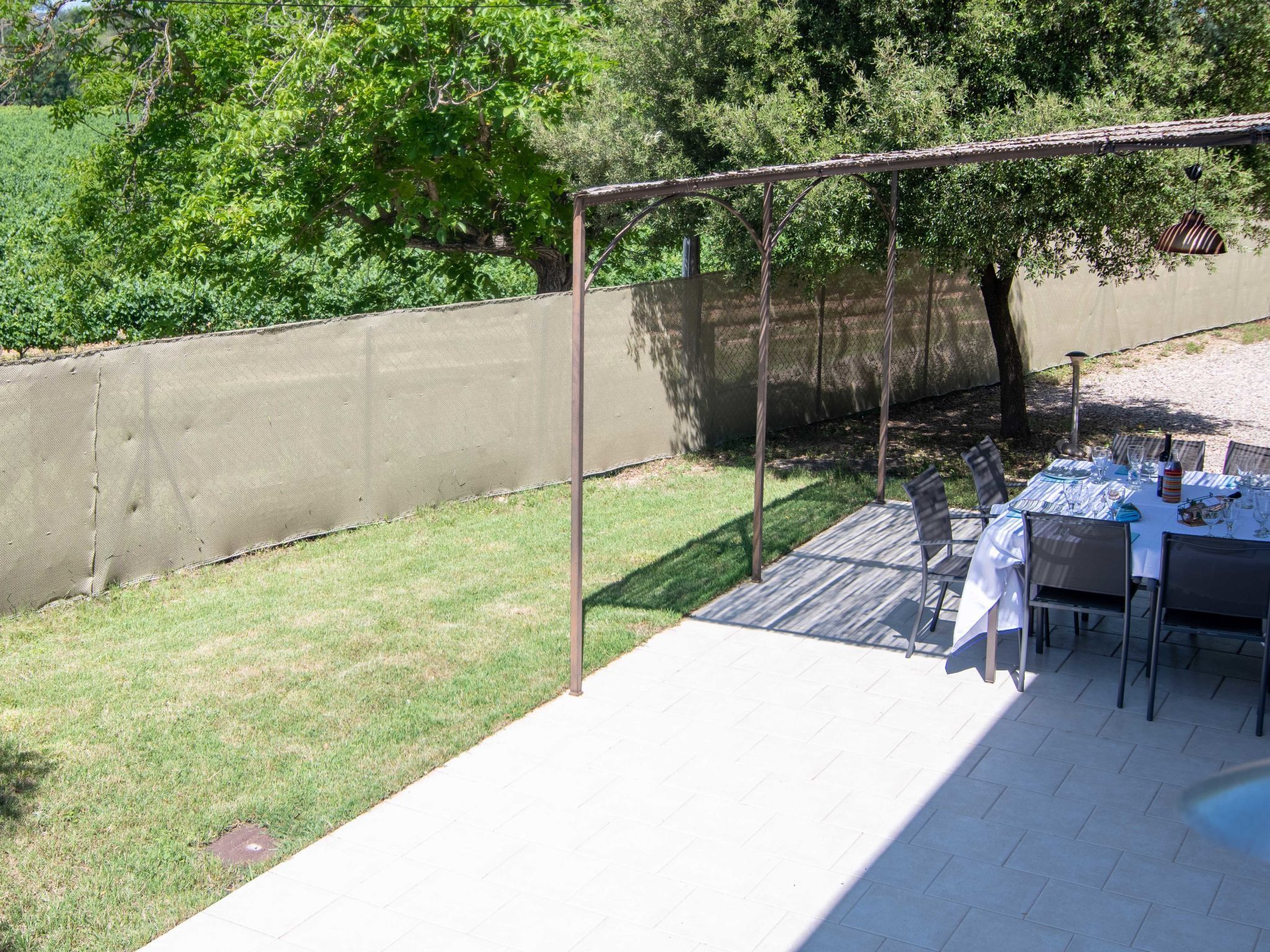 An outdoor patio with a table set for dining, surrounded by chairs, and a pergola structure.
