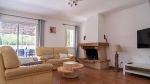 Ett vardagsrum med en beige soffa, ett runt soffbord, en öppen spis och en tv som är monterad på väggen.