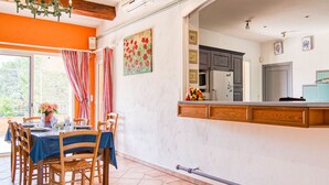 A dining area with a table set for four, a chandelier, and a view of the kitchen.