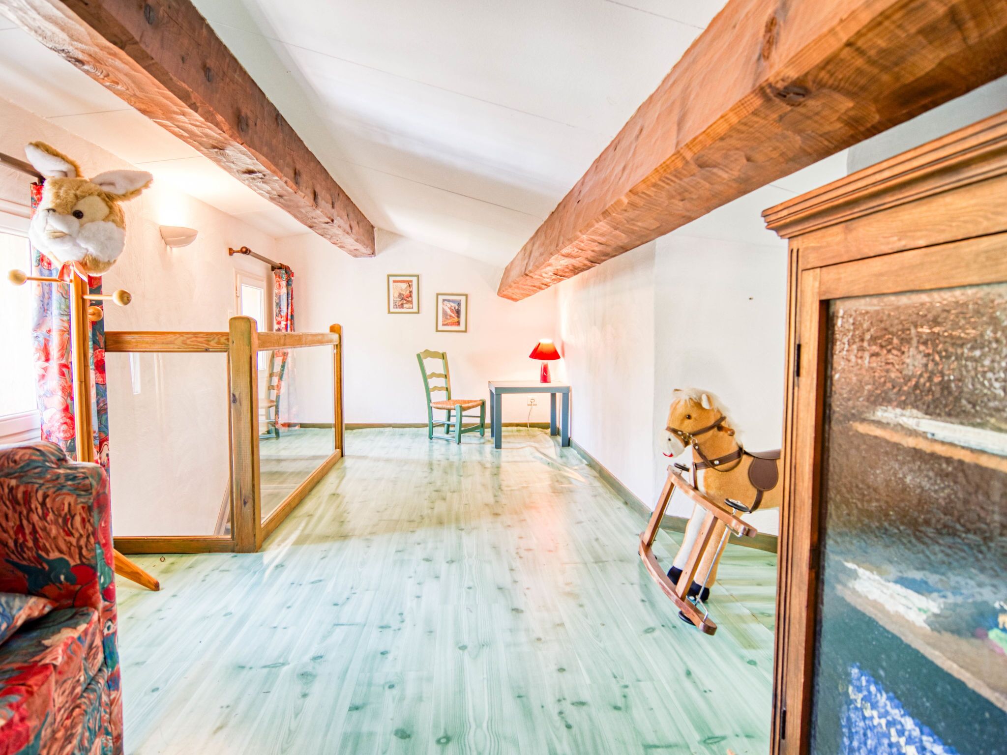 A room with wooden beams, a rocking horse, a chair, a table, and a mirror.