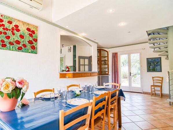 A dining area with a table set for four, wooden chairs, a cabinet with glass doors, a painting on the wall, and a staircase to the right.