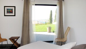 A bedroom with a bed, two chairs, a window with curtains, and a framed picture on the wall. - Baie de Bandol by Interhome (Sanary sur Mer)